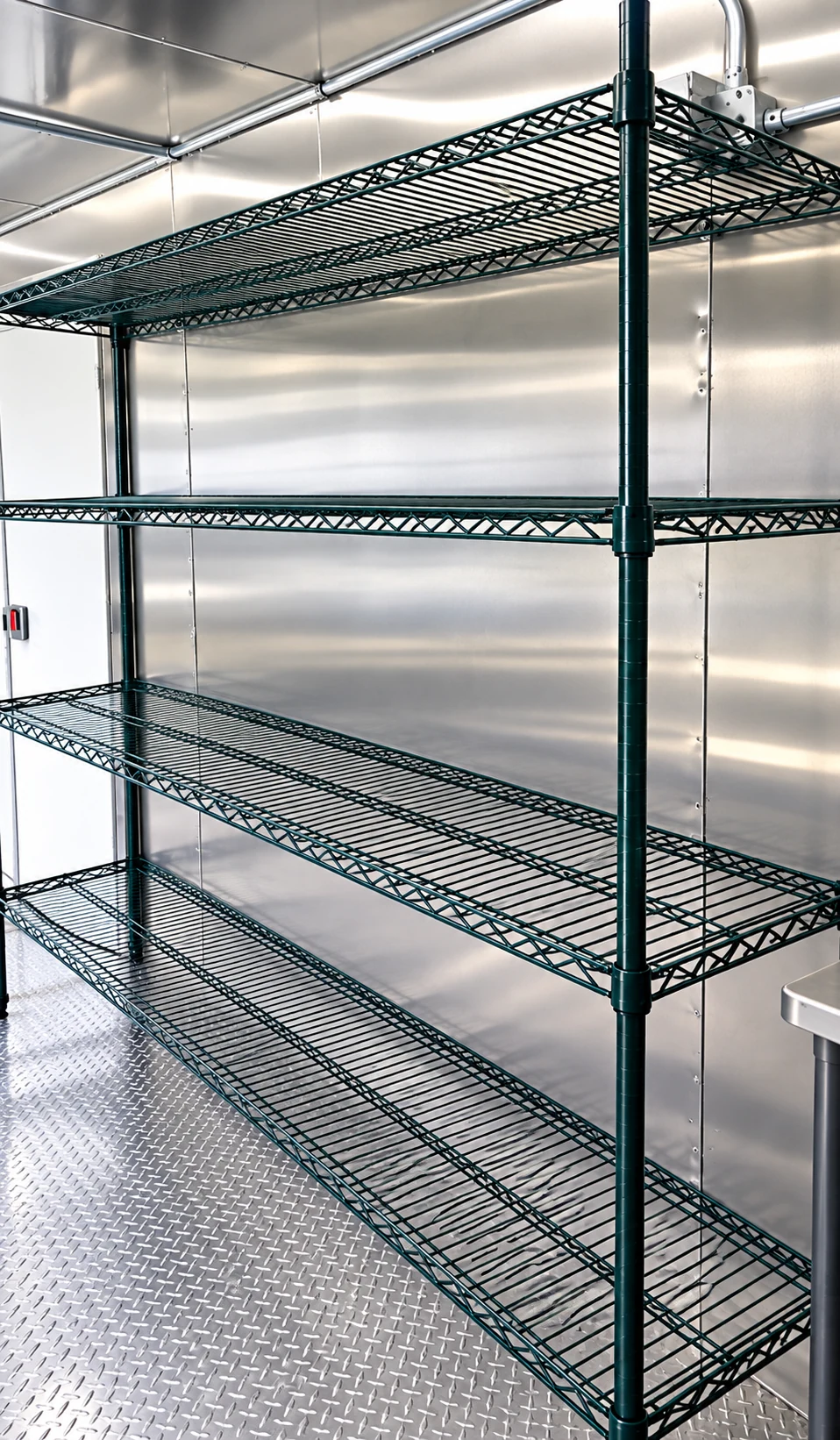 Green wire shelving racks standing empty on a stainless floor inside a dishwashing trailer